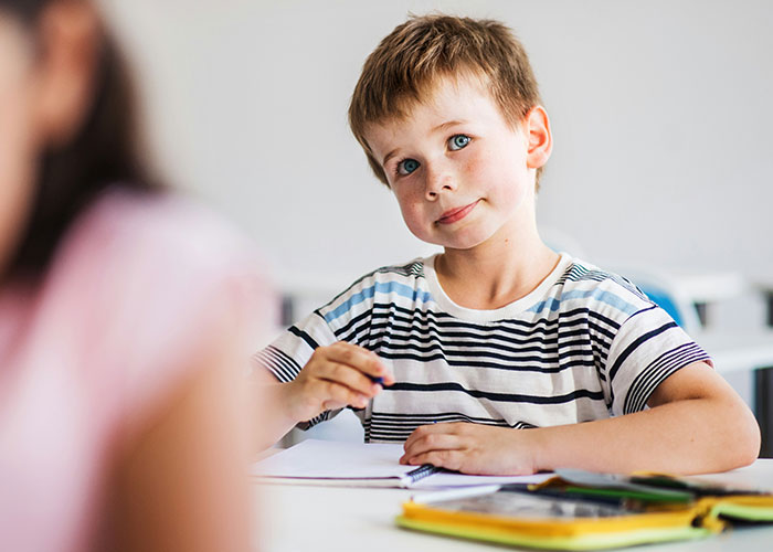 Young boy sitting at a desk looking thoughtful while writing, representing school punishments that upset people. - 13