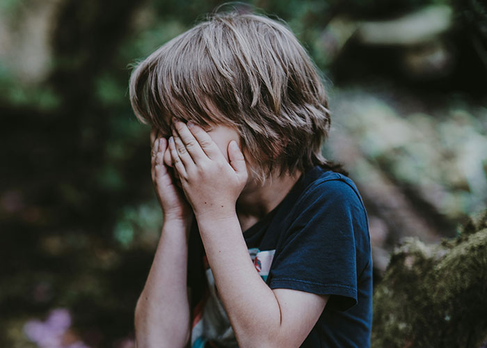 Young child covering face outdoors, reflecting emotions related to being punished at school for various things. - 23