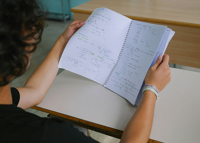 Student sitting at a desk, holding a notebook with handwritten school notes, reflecting on things punished at school. - 5