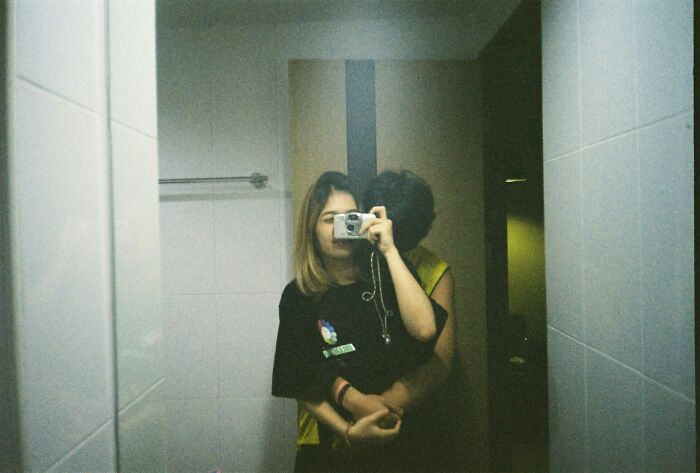 Couple embracing in front of bathroom mirror capturing a photo, illustrating pettiest things in breakups and borderline insane moments.