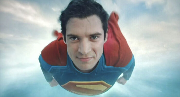 Superman in blue and red costume flying forward with determined expression in a scene from the woke Superman reboot.