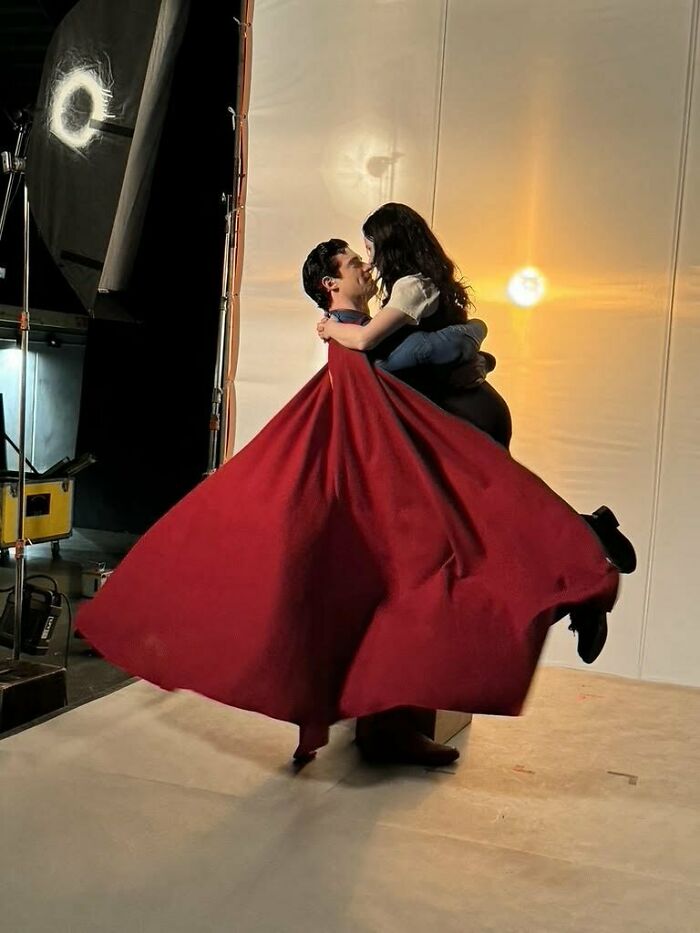 Superman reboot photoshoot with actor in red cape holding a woman, showcasing the film&rsquo;s new look for woke Superman.