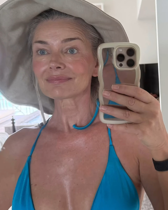 Supermodel at 60 taking a selfie wearing a hat and blue swimsuit, showing natural skin without filters. - 9