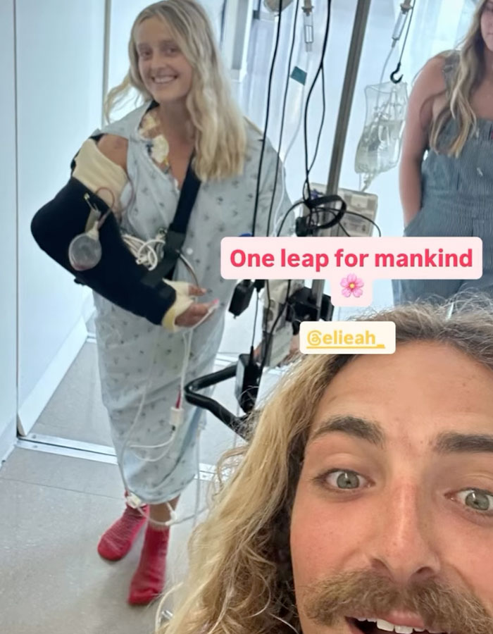 Young surf instructor in hospital gown with arm in a cast and sling, smiling during recovery after train accident.