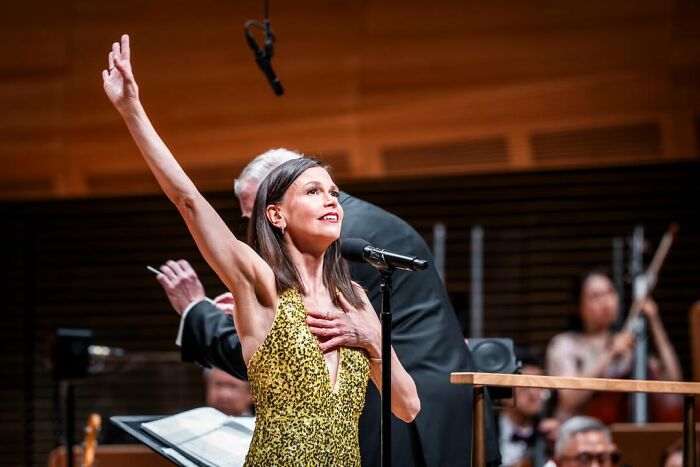 Female singer in a gold dress performing on stage with musicians in the background, showcasing emotional expression during a concert.