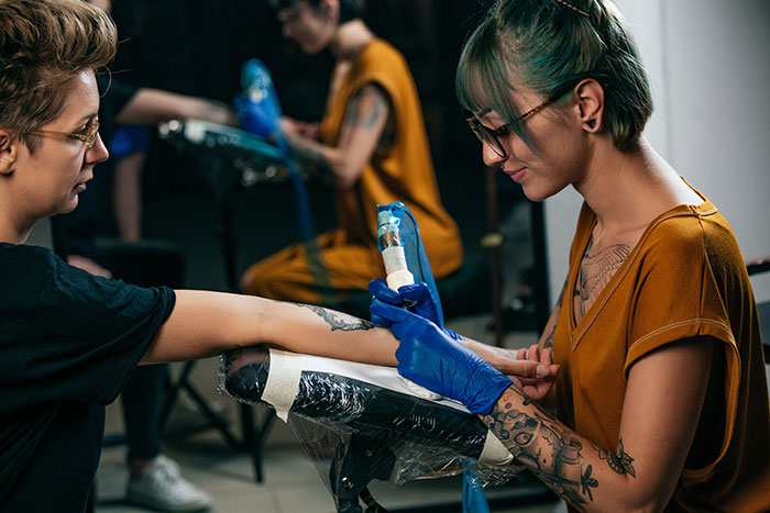 Tattoo artist wearing gloves carefully working on a client’s forearm in a studio focused on moral grounds.