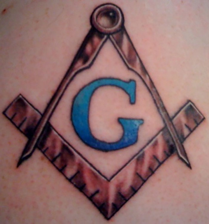 Tattoo of a blue G inside a brown square and compass symbol, representing jobs some tattoo artists decline on moral grounds.
