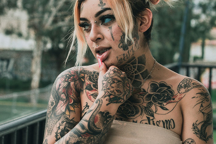 Woman with extensive tattoos on face, neck, and arms, representing tattoo artists who decline jobs on moral grounds.