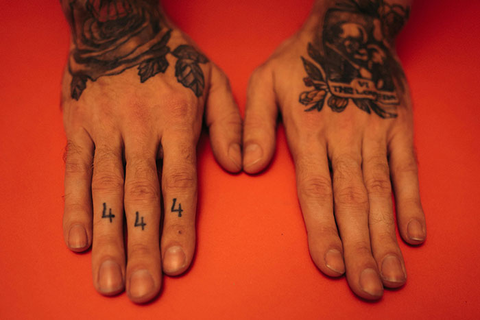 Close-up of tattooed hands on an orange background, illustrating tattoo artists' choices on jobs they decline on moral grounds.