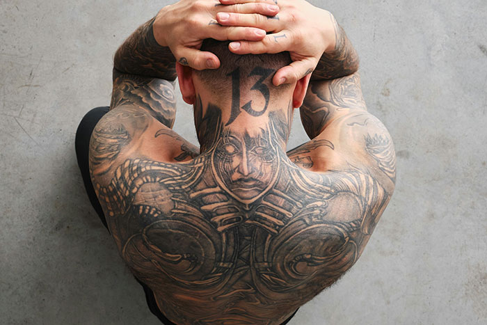 Tattoo artist with intricate back and neck tattoos showcasing designs they may decline based on moral grounds.
