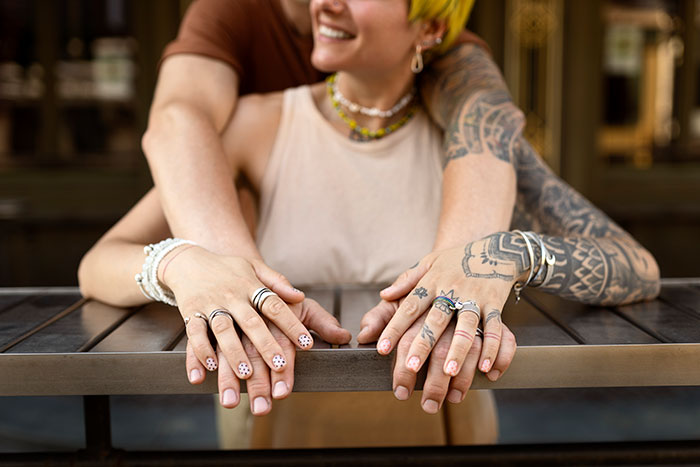 Young tattooed person with brightly colored hair smiling while holding hands with partner, showcasing tattoo artists' moral choices.