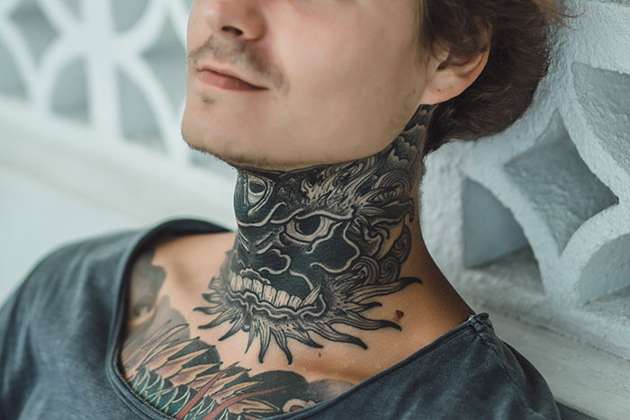 Young man with intricate dragon neck tattoo and chest ink, showcasing bold tattoo art by skilled tattoo artists.