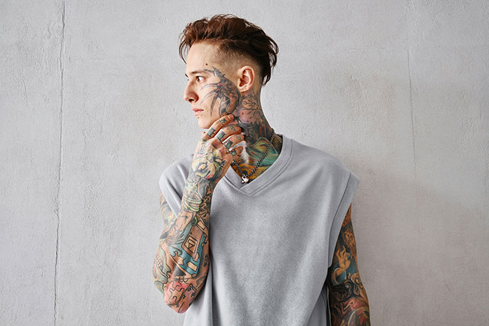 Tattoo artist with full sleeve and neck tattoos wearing gray sleeveless shirt, symbolizing jobs declined on moral grounds.