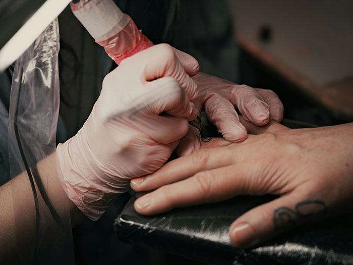 Tattoo artist wearing gloves carefully working on a hand tattoo, illustrating jobs declined on moral grounds.