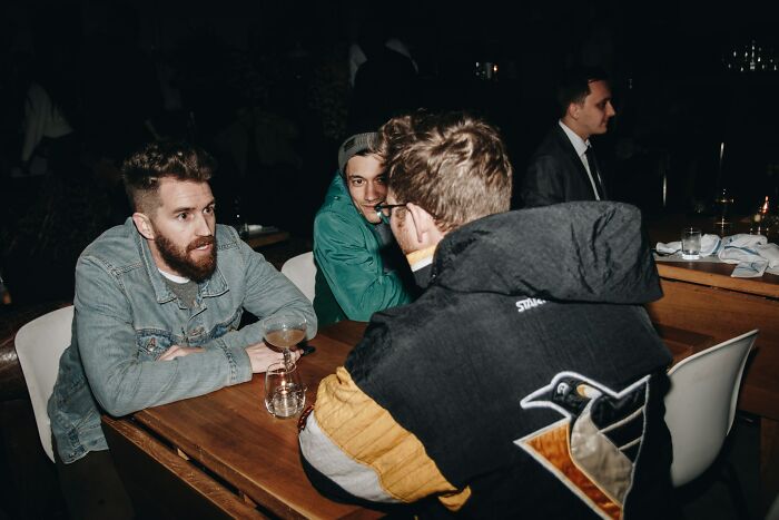 Three men sharing a conversation at a dimly lit bar, illustrating things normal to men but bizarre to women.