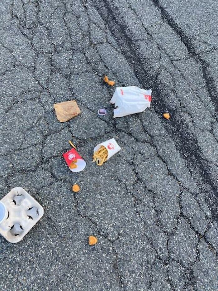 Fast food delivery spilled on c*****d asphalt, highlighting unfortunate package delivery mishaps off track.