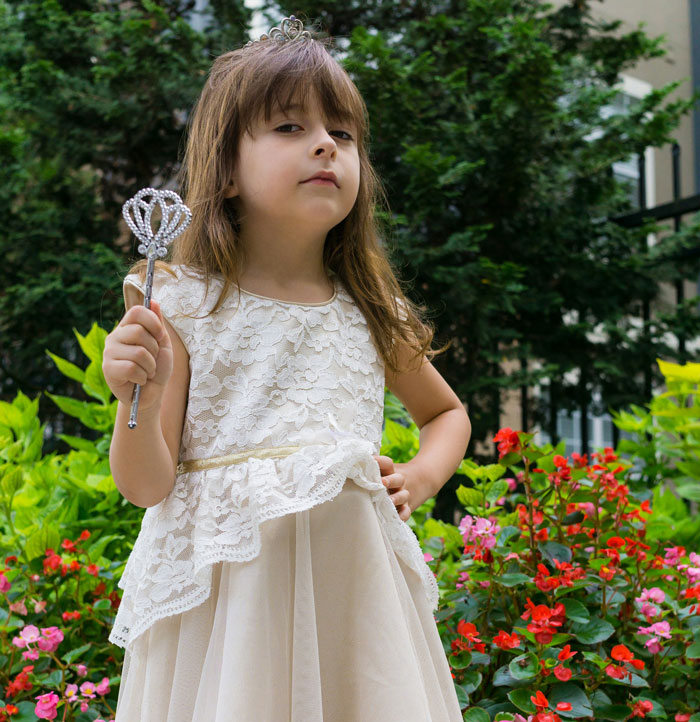 Young girl in a white dress holding a wand, representing adoption and parents playing favorites in an outdoor garden setting.
