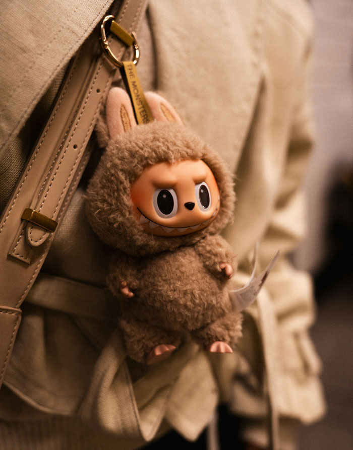 Plush toy keychain attached to a beige bag, highlighting family dynamics of parents playing favorites and adopted daughter moving out.