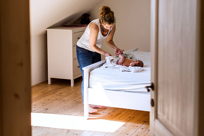 Teen changing a baby on a bed, illustrating the concept of refusing to be a live-in babysitter for parents. - 5