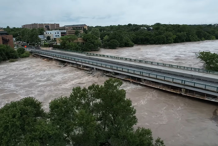 Flood victim message revealed as swollen river rushes beneath a bridge amid severe flooding and damage to infrastructure.