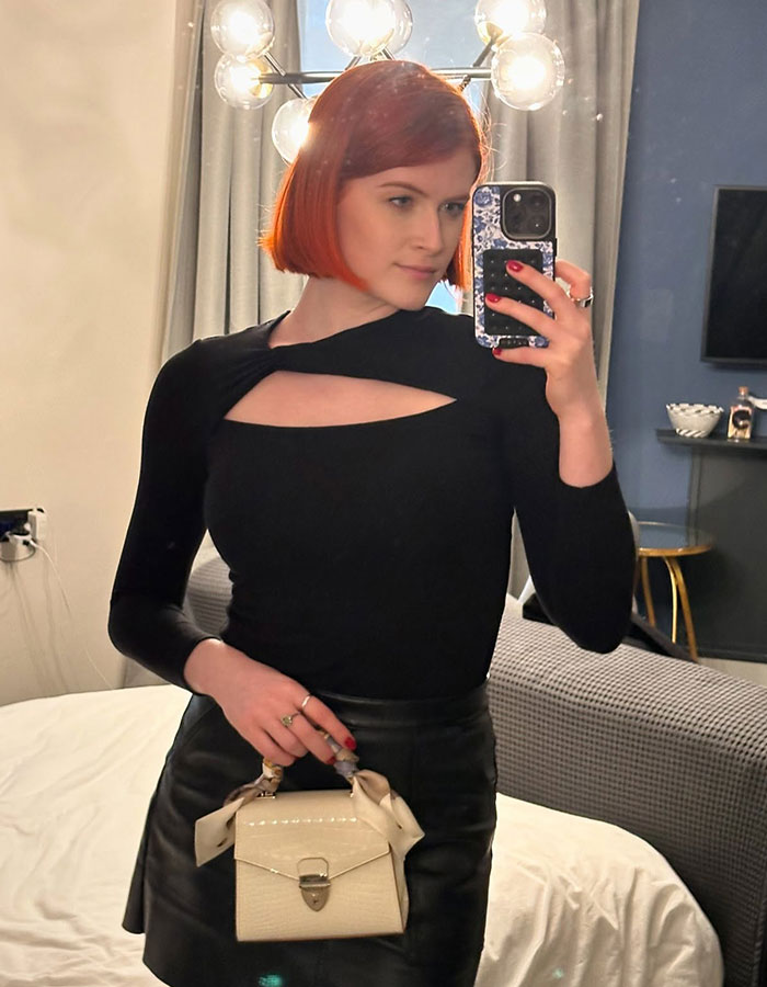 Professional escort taking mirror selfie in black outfit, highlighting challenges of racial discrimination in the industry.
