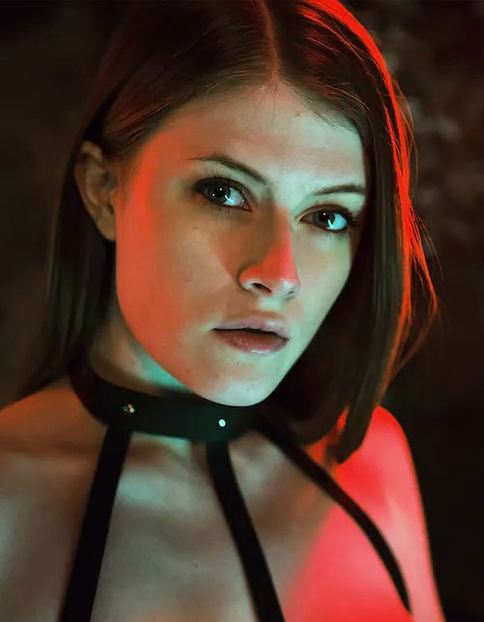 Young woman with serious expression in moody lighting, representing professional escort facing racial discrimination in the industry.