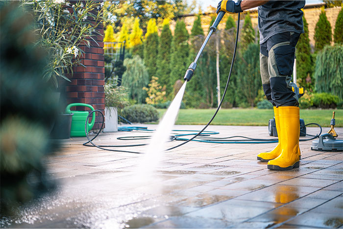 Person wearing yellow boots pressure washing a patio, illustrating seemingly innocent things that are deadly risks in home care.