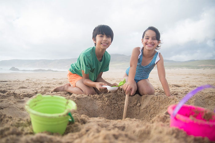 Two children playing with sand toys at the beach, highlighting seemingly innocent things that are deadly risks to kids.