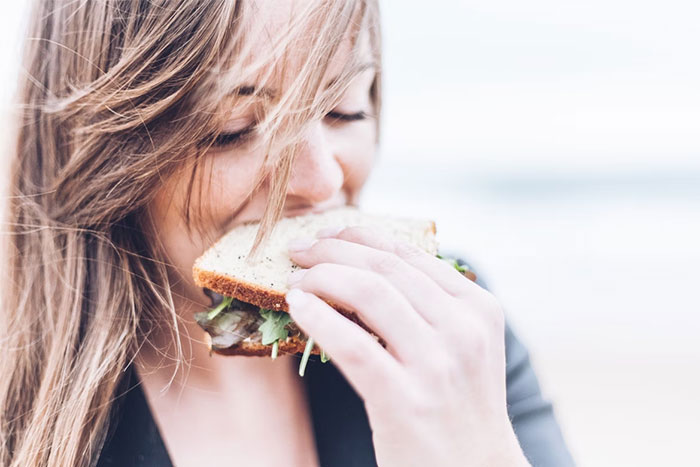 Young woman eating a sandwich outdoors, illustrating seemingly innocent things that are deadly in everyday life.