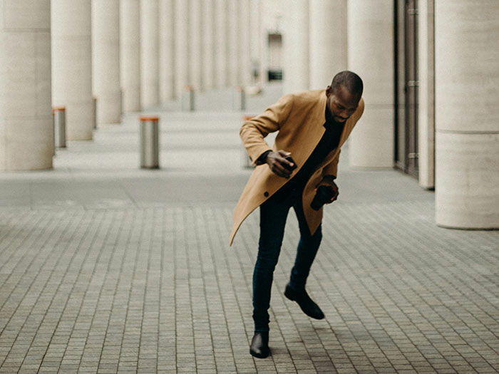 A man in a brown coat slipping on a pavement with tall columns in the background, showing seemingly innocent things that are deadly.
