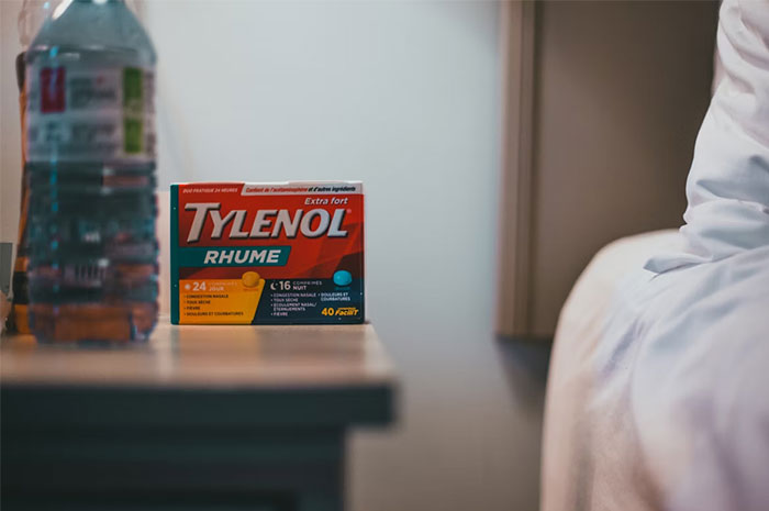 A box of Tylenol on a bedside table next to a water bottle in a bedroom setting with soft natural light.