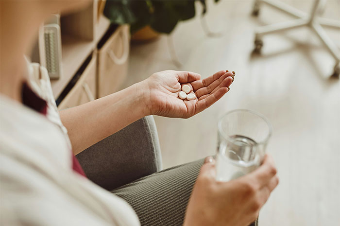 Person sitting with white pills in one hand and holding a glass of water, illustrating seemingly innocent things that are deadly.
