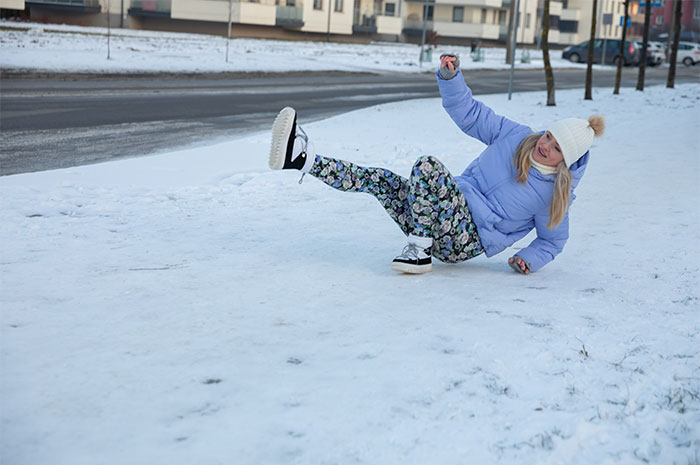 Woman slipping on icy snow-covered ground wearing winter clothes, illustrating seemingly innocent things that are deadly.
