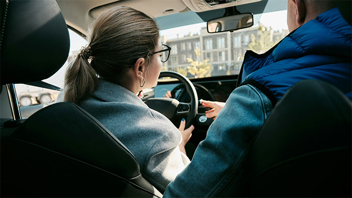 Woman driving a car while receiving instructions from a passenger, highlighting deadly seemingly innocent things on the road.