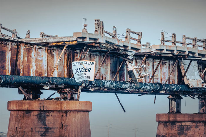 Rusty old bridge with a danger sign warning of falling debris, illustrating seemingly innocent things that are deadly.