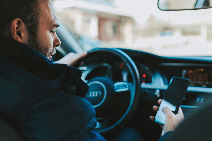 Man in a car using a smartphone while driving, illustrating one of the seemingly innocent things that are deadly risks.