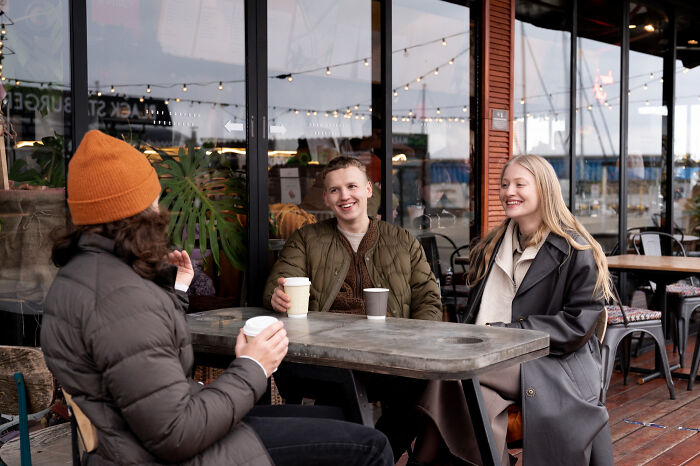 Three friends enjoying coffee and conversation outdoors, reflecting trust and patience from the good old days disappearing.