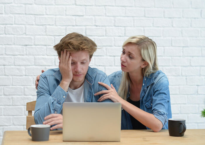 A woman comforting a stressed man working on a laptop, highlighting trust and patience slowly disappearing from the good old days.
