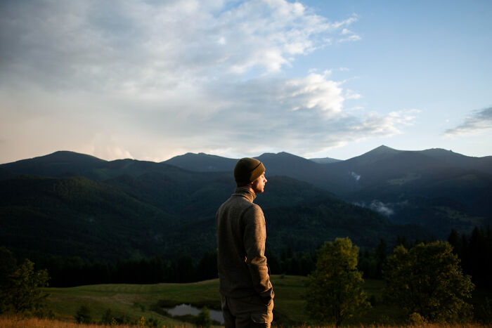 Man wearing a beanie standing in a peaceful mountain landscape reflecting on trust and patience from the good old days.