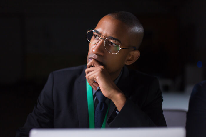 Man with glasses and green lanyard, dressed in a suit, thoughtfully reflecting on trust and patience from the good old days.