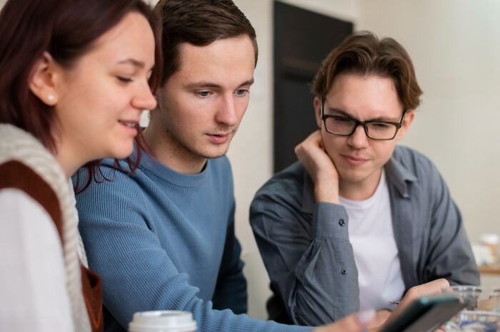 Three young adults focusing on a smartphone, reflecting trust and patience from the good old days slowly disappearing.