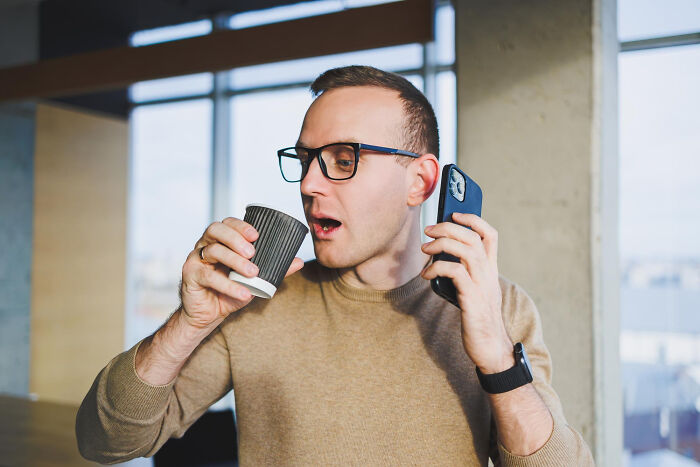 Man wearing glasses holding a phone and a paper cup, representing trust and patience slowly disappearing from old days.