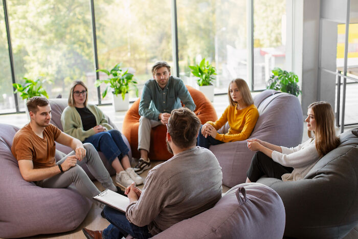 Group of people sitting on bean bags in a bright room, engaged in a discussion about trust and patience fading from the old days.
