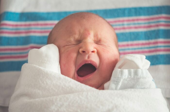 Newborn baby wrapped in a white blanket yawning, illustrating common challenges women face after birth.