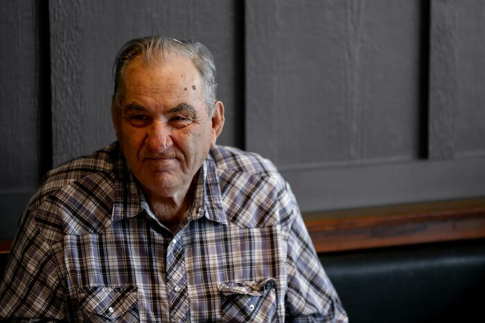 Elderly man in a plaid shirt sitting alone, reflecting on relationship struggles and partner's shenanigans before leaving.