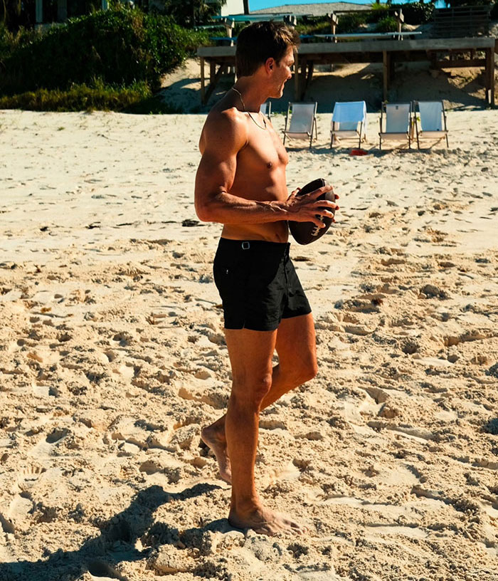 Shirtless man playing with a football on a sunny beach, capturing summer romance and spice vibes outdoors.