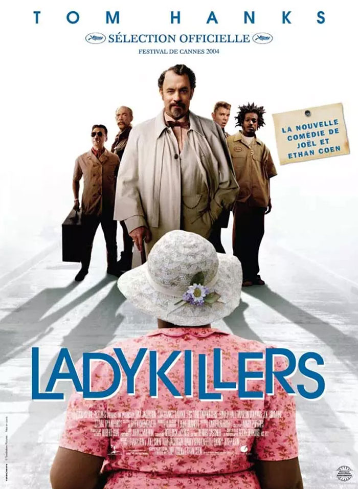 Tom Hanks in a scene from Ladykillers, featuring a group of men standing behind a woman in a pink hat and dress.