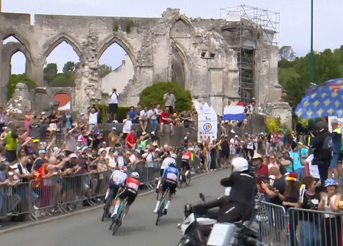 Tour De France fans crowd the roadside and stand on graves at a historic site to get a better view of the race.