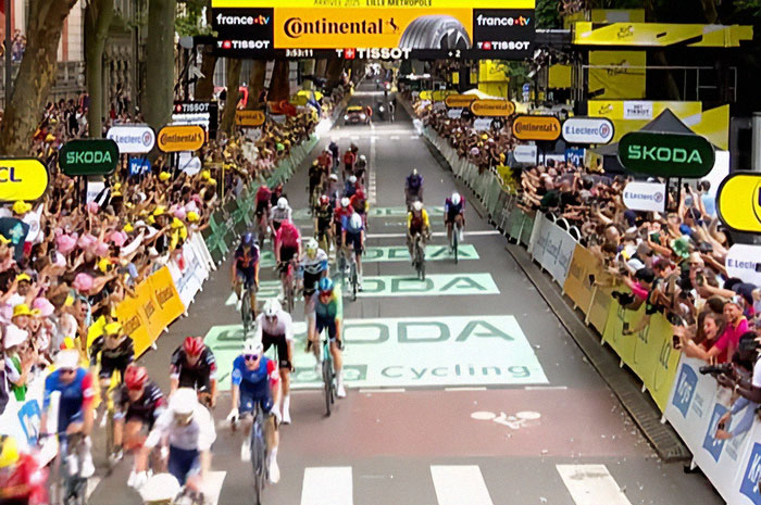Cyclists racing at Tour De France finish line with crowds standing on graves for better view causing outrage.