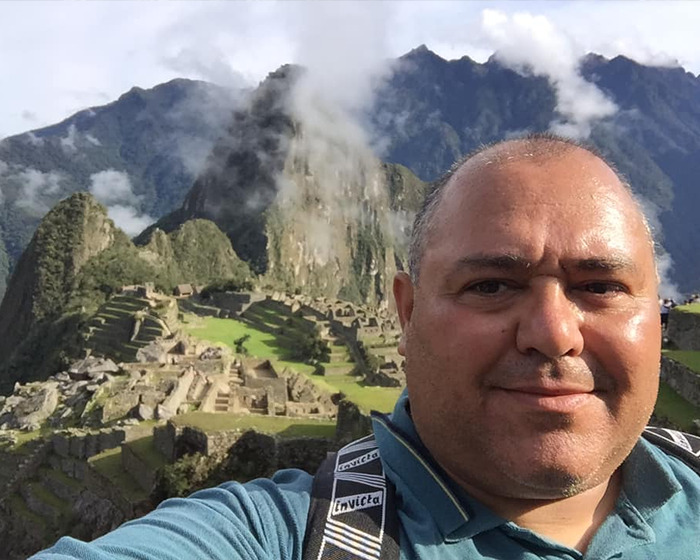 Tourist taking selfie near cliff warning signs with mountainous landscape in background, bear drags off cliff incident concept.